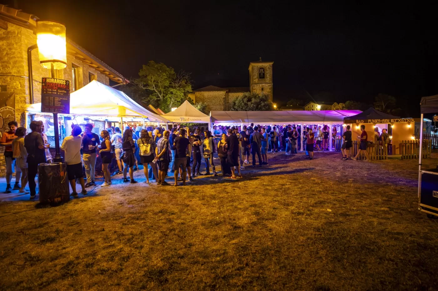 Recinto de Pikotako iluminado de noche con público entre las carpas