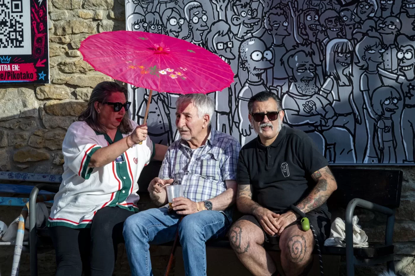 Tres asistentes descansando bajo una sombrilla rosa